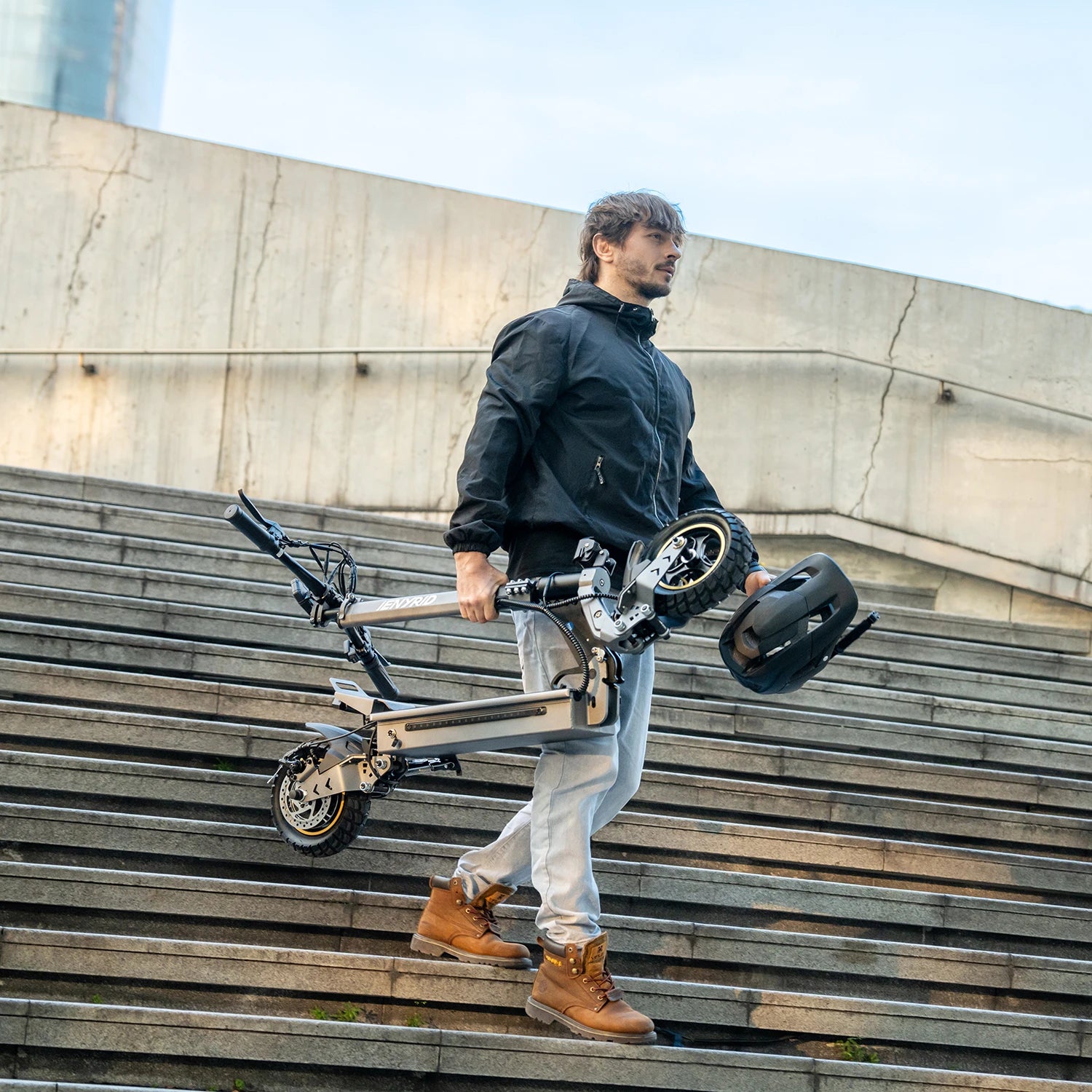 Man carrying a folded electric scooter up outdoor steps.